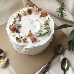 a cake with white frosting and flowers is on a table next to spoons