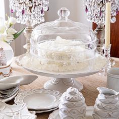 a cake on a platter surrounded by white dishes and silverware, with crystal chandelier in the background