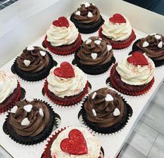 twelve cupcakes with chocolate frosting and hearts on top are in a box