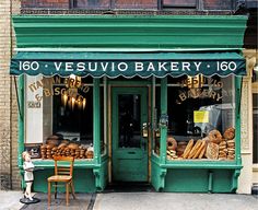 a store front with green awnings and bread on display in the window next to a wooden chair