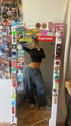 a woman taking a selfie in front of a mirror covered in stickers and magnets