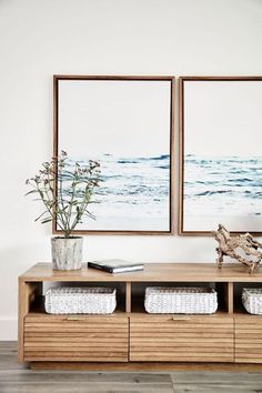 two framed pictures hang on the wall above a wooden table with baskets and vases