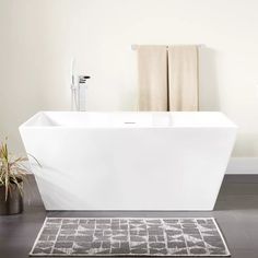 a white bath tub sitting on top of a bathroom floor next to a potted plant