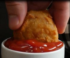 a person dipping something into a small white bowl with ketchup on it's side