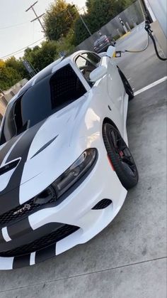 a white car with black stripes on it's hood parked in front of a gas station