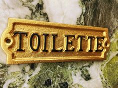 a gold sign that reads toilet on it's side next to a marble wall