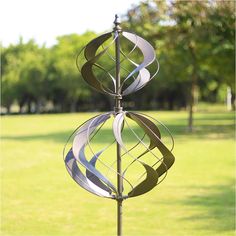 a metal wind spin in the middle of a grassy area with trees and grass behind it