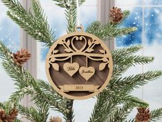 a wooden ornament with two hearts hanging on a christmas tree in front of a window