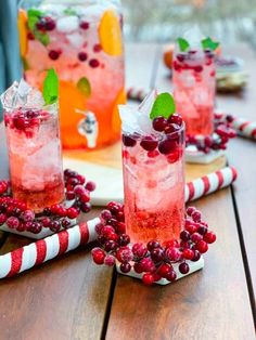 three glasses filled with cranberry punch sitting on top of a wooden table next to candy canes