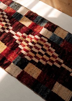 a red, yellow and blue rug sitting on top of a wooden floor next to a window