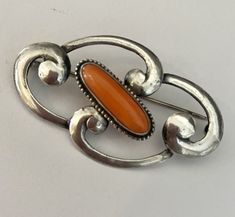 Fabulous! Beautiful sterling silver swirls define the the Art Nouveau era. The centerpiece of this brooch is an elongated cabochon natural coral. This brooch looks gorgeous pinned on a simple velvet choker.  Marked STERLING Elegant Sterling Silver Brooch With Cabochon, Elegant Orange Brooch Jewelry, Orange Brooch Jewelry For Formal Occasions, Formal Orange Brooch Jewelry, Elegant Orange Brooches For Gifts, Elegant Oval Sterling Silver Brooches, Velvet Choker, Natural Coral, Tatting