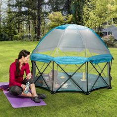 a woman sitting on top of a purple mat next to a blue and white tent