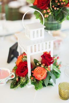 a white lantern with red and orange flowers on it sitting on a table next to a vase