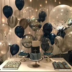 a table topped with lots of blue and white balloons next to a cake covered in confetti