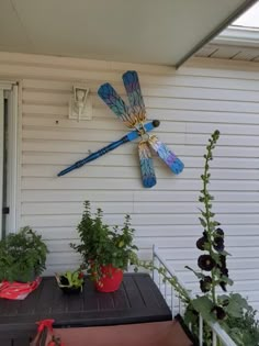 a blue dragonfly clock mounted on the side of a white house next to potted plants