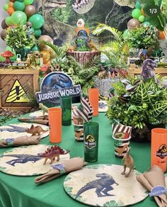 a green table topped with plates covered in food and dinosaurs on paper napkins next to plants