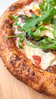 a close up of a pizza on a cutting board with green toppings and leafy greens