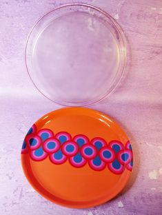 an orange and blue plate sitting on top of a purple tablecloth next to a clear bowl