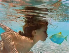 a woman swimming under water next to a blue fish