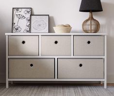 a white dresser with four drawers next to a lamp and pictures on the wall above it