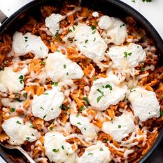 a skillet filled with pasta and cheese on top of a white table next to parsley