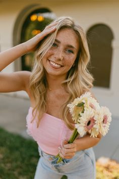 a beautiful young blonde woman holding a bouquet of flowers in front of her face and smiling at the camera