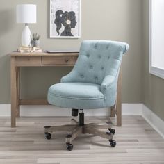 a blue office chair sitting on top of a wooden desk next to a painting and lamp