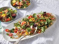 two plates filled with salad on top of a white table cloth next to water glasses