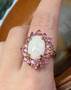 Vintage Natural Australian Fire Opal surrounded by 24 small pink tourmaline gemstones. Cabochon Ring.  Set in solid 14K yellow gold. Stamped "14k China" Currently at a size 8, can be resized upon request.  Opal has no flaws or chips. Weight: 5 g Size: 8 US Ring resizing is complimentary, if the ring design might be compromised during resizing the seller will contact you. Please contact seller if you have any questions or want more details. Many of our pieces are irreplaceable so merchandise over $100 will be shipped fully insured and signature required for delivery when applicable so that we can ensure our customer receives their order. If you'd prefer to not to require signature please contact seller. If you'd prefer your item to be shipped with recycled or plastic free packaging, just le Pink Oval 14k Stamped Jewelry, Pink 14k Stamped Jewelry For Wedding, 14k Stamped Oval Pink Jewelry, Pink 14k Stamped Wedding Jewelry, Pink Heirloom Birthstone Jewelry, Pink Opal Gemstone Ring For Anniversary, Formal Pink Oval Opal Ring, Pink Opal Ring For Anniversary, Pink Cluster Jewelry With Accent Stones