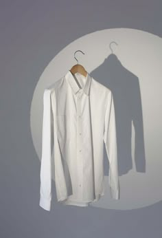 a white shirt hanging on a hanger in front of a gray wall with the shadow of a man's head