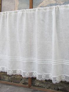 a white curtain hanging on the side of a window next to a stone wall with two pictures behind it