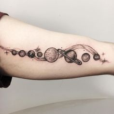 an arm tattoo with planets and stars on the outer half of it, in black ink