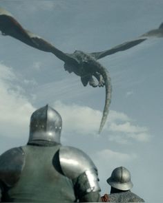 two men in armor look at a dragon flying over them