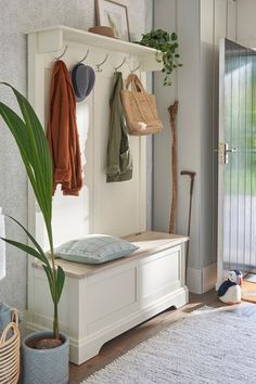 a white bench sitting under a window next to a potted plant and coat rack