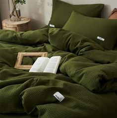 an open book is laying on a bed with green sheets and pillows in the corner