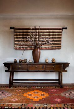 a wooden table topped with a vase filled with flowers next to a wall mounted art piece