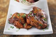 two pieces of meat on a white plate with a fork in it and a small bowl of sauce