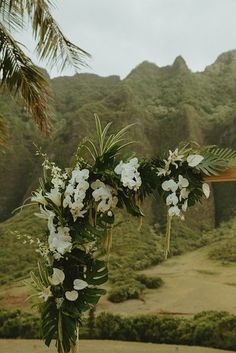 a vase filled with white flowers sitting on top of a wooden table next to a lush green hillside