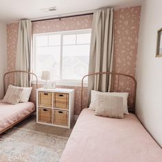 two twin beds in a small room with pink walls and floral wallpaper on the walls