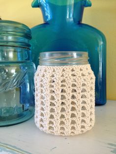 a crocheted jar cover sitting on top of a table next to blue jars