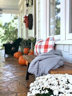 a wooden bench sitting on the side of a building next to flowers and pumpkins