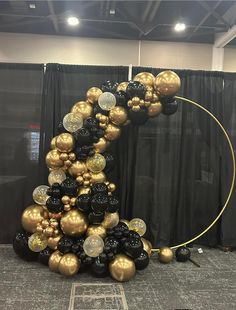 black and gold balloons are arranged in the shape of a letter on a round stand