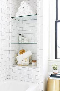 a white tiled bathroom with glass shelves above the bathtub and towels on the shelf