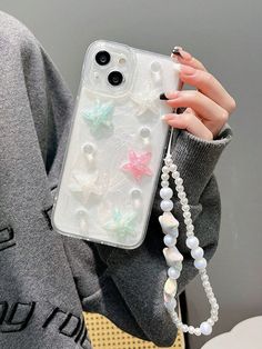 a woman holding up her phone case with pearls and stars on it, while wearing a gray sweater