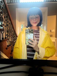 a woman taking a selfie in front of a mirror with her cell phone and wearing a yellow raincoat