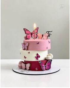 a three tiered cake with pink butterflies on it and a lit candle in the middle