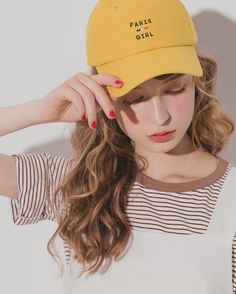 a woman wearing a yellow hat with the words paris girl on it, standing against a white wall