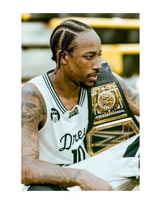 a man with dreadlocks sitting on a bench holding a gold and black belt