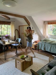 a woman walking across a living room with a bed and desk in front of her