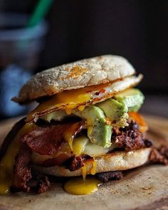 a sandwich with bacon, cheese and avocado on it sitting on top of a wooden cutting board